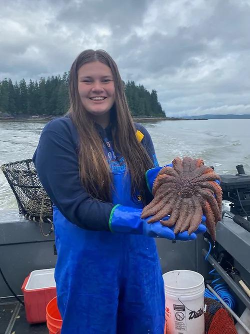 Alyssa Guthrie on a boat outside her hometown of Petersburg Alaska holding a sunflower sea star
